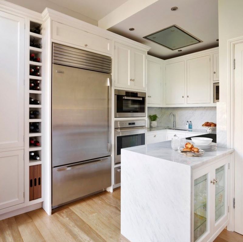 Белый кухонный гарнитур и холодильник с отделкой из нержавеющей стали