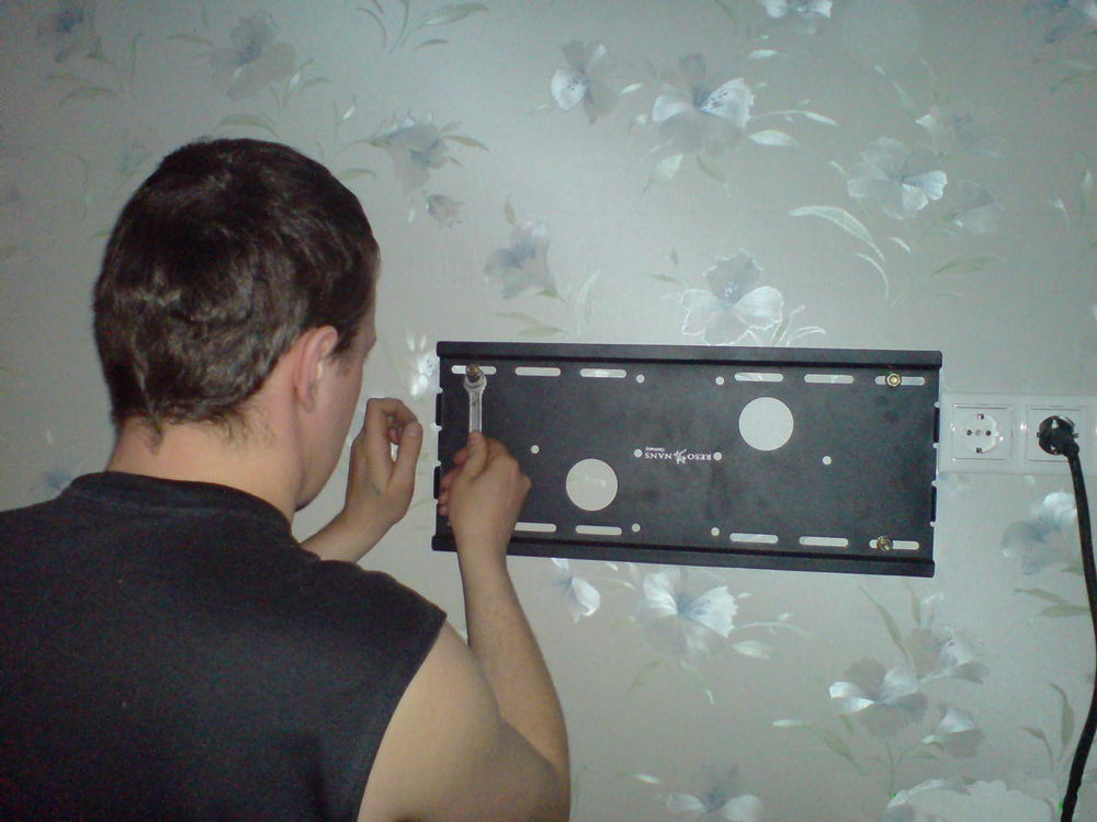 Мужчина устанавливает кронштейн для телевизора на стену